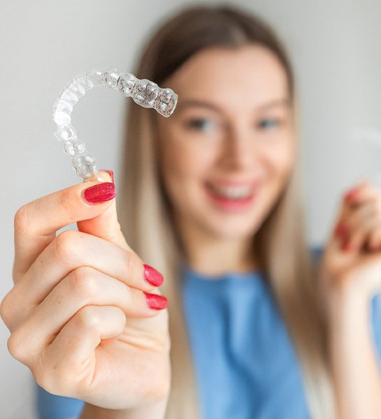 Woman in blue shirt with red nails holding 2 Invisalign trays