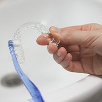 Hands brushing Invisalign with small toothbrush