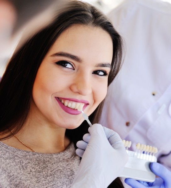 Dentist holding shade options next to smile of young woman in dental chair