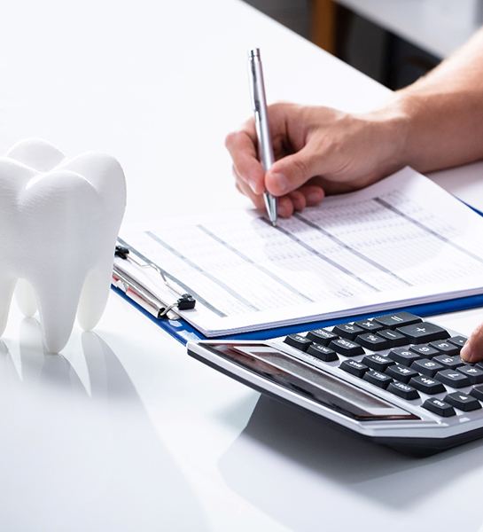 Model of tooth with calculator on desk of person calculating the cost of cosmetic dentistry in Naples