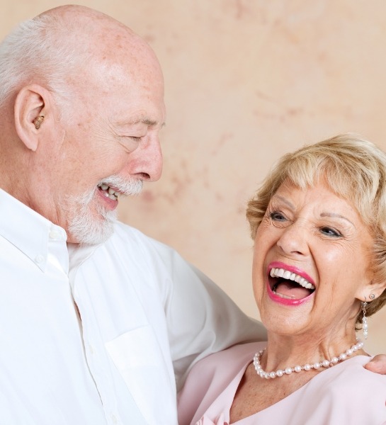 Man and woman with flawless smiles after dental implant supported denture placement