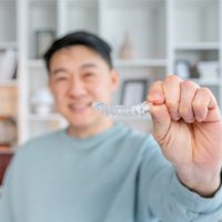 Closeup of smiling patient holding Invisalign aligner