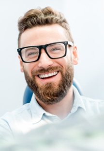 Man with glasses sitting in dental chair and smiling