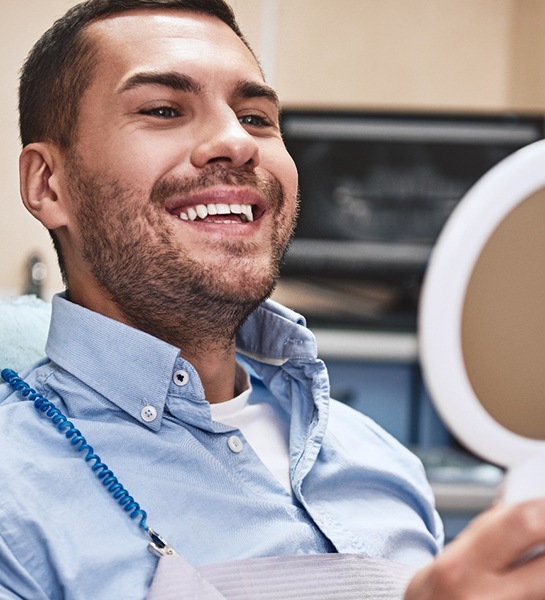 Male dental patient looking at his smile in a handheld mirror