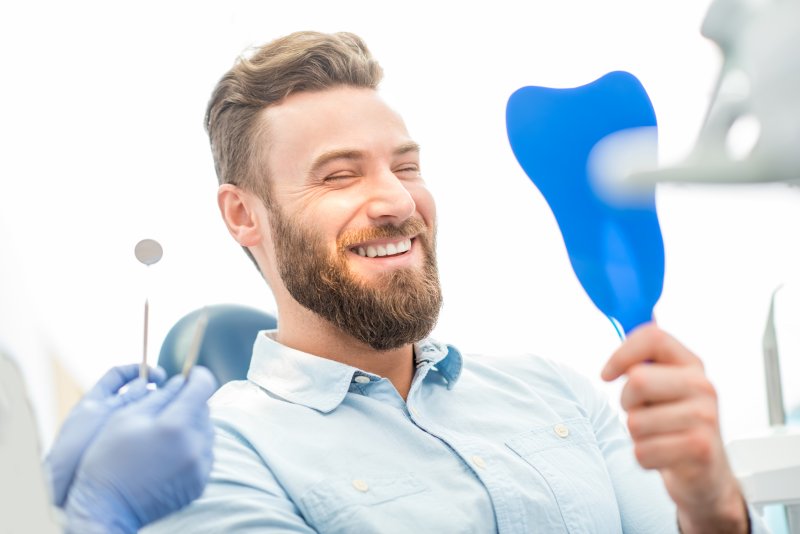 A male dental patient smiling in front of a hand mirror
