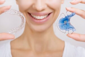 Nose-to-shoulder view of woman holding up 2 types of retainers