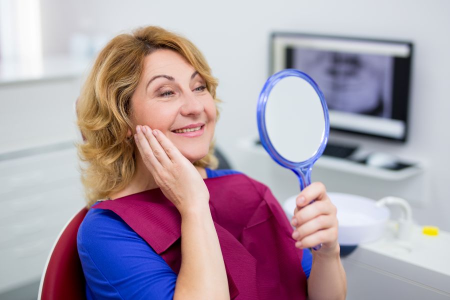 A woman looking at her new dental implants in a mirror.